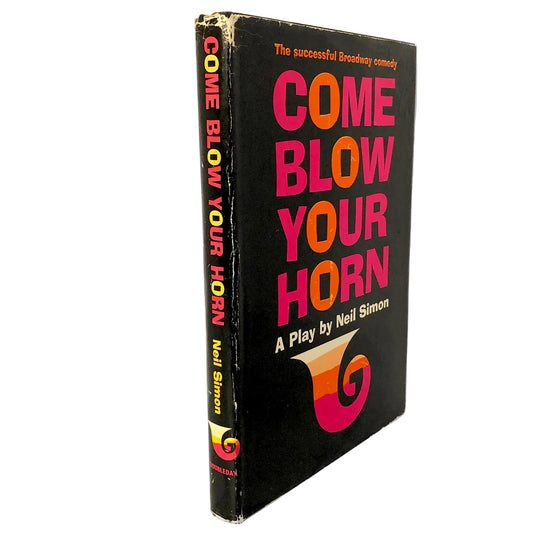 A vintage hardcover book titled 'Come Blow Your Horn' by Neil Simon, standing upright on a light marble surface against a white background. The cover is black with bold pink, orange, and yellow lettering.