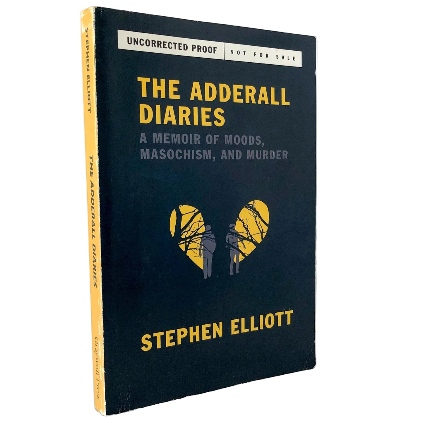 The Adderall Diaries book by Stephen Elliott, standing upright on a marble surface against a white wall. The book cover is dark navy blue with yellow and gray text, and a yellow heart-shaped graphic in the center.