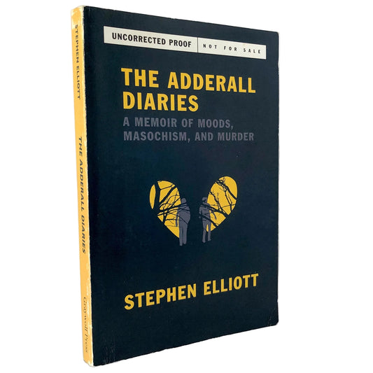 The Adderall Diaries book by Stephen Elliott, standing upright on a marble surface against a white wall. The book cover is dark navy blue with yellow and gray text, and a yellow heart-shaped graphic in the center.