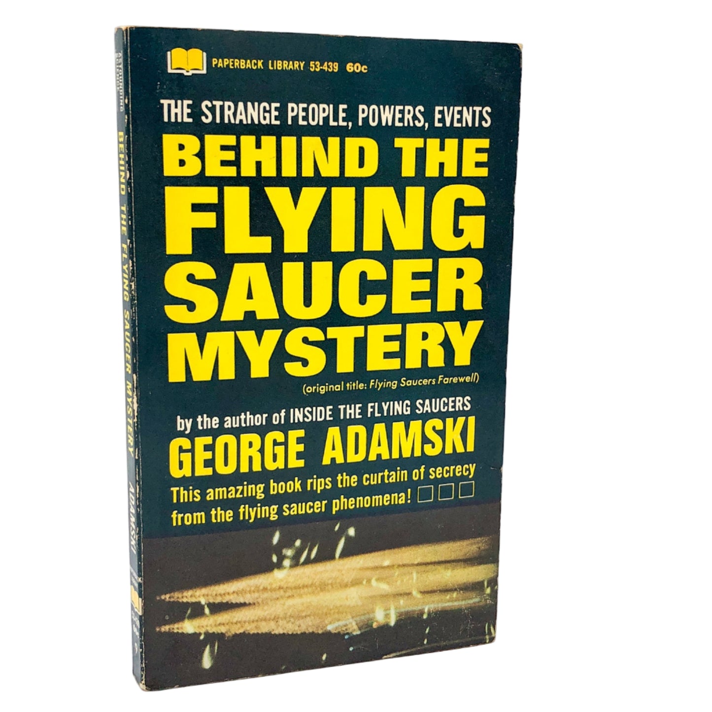 The image displays the paperback edition of "Behind the Flying Saucer Mystery" by George Adamski, first published in 1967. The book's cover features a striking, vivid illustration of a flying saucer in mid-flight, with a backdrop of a stormy night sky.