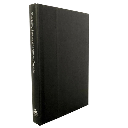 A black hardcover book standing upright on a light marble surface against a white background. The spine is visible and reads 'The Early Stories of Truman Capote' with a small publisher logo near the bottom.