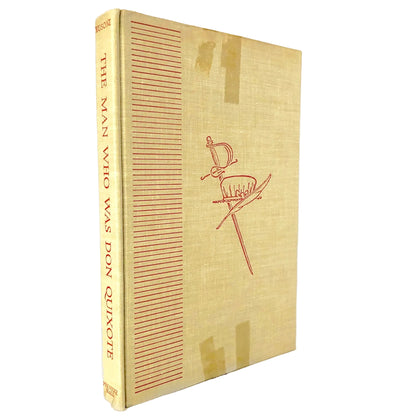 Vintage hardcover book titled 'The Man Who Was Don Quixote' with a tan linen cover and red line art of a sword, standing on a white background with a marble surface.
