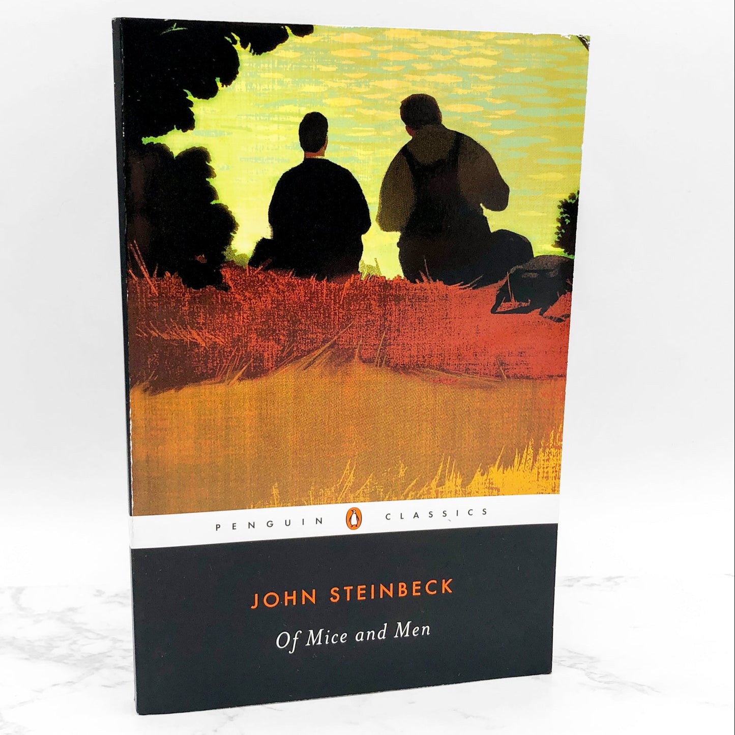 Trade paperback cover of 'Of Mice And Men' by John Steinbeck, published by Penguin Classics, with an illustration of two men in a field at dusk.