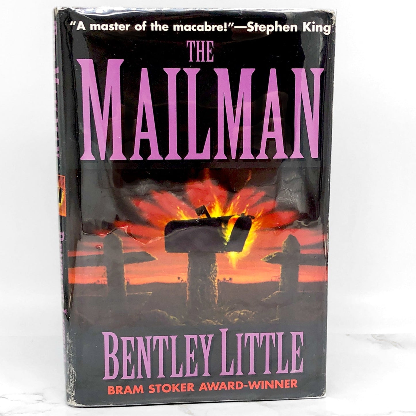 The cover of 'The Mailman' book by Bentley Little features a silhouette of a mailman with a dark, ominous background. The book is a horror novel and has won a Bram Stoker Award.