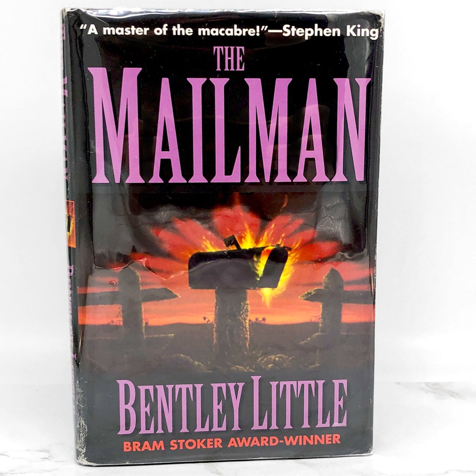 The cover of 'The Mailman' book by Bentley Little features a silhouette of a mailman with a dark, ominous background. The book is a horror novel and has won a Bram Stoker Award.
